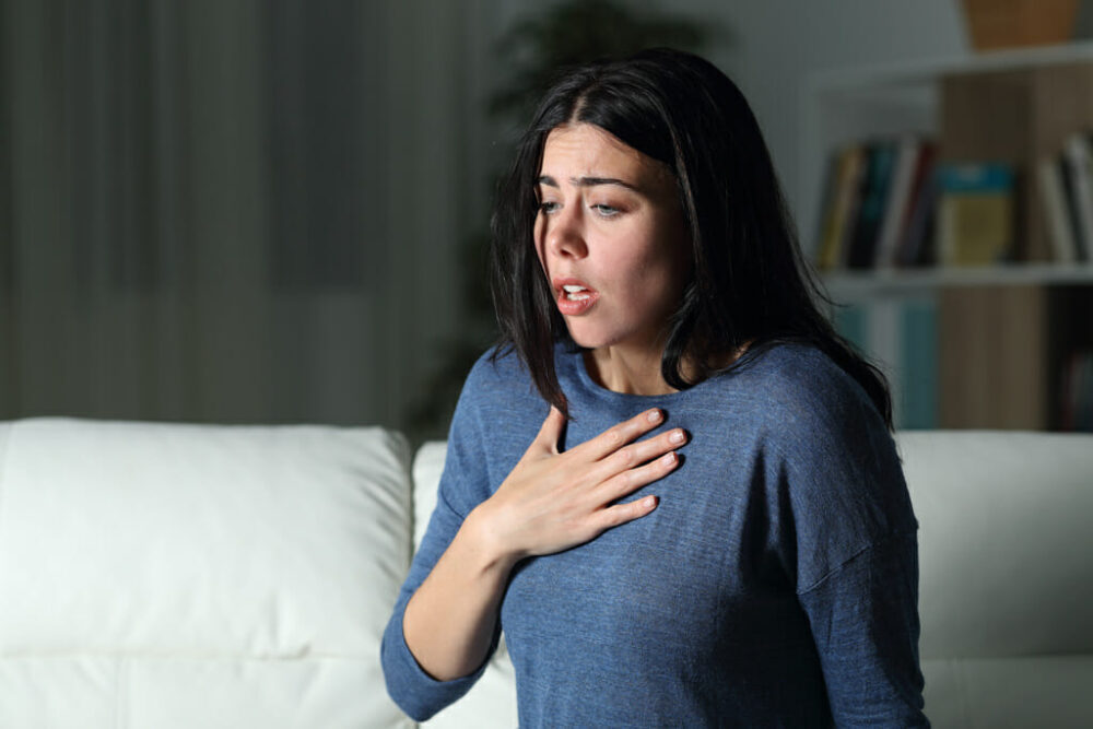 Woman suffering from shortness of breath whilst sitting on her sofa