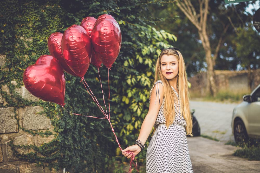 a woman smiling whilst holding balloons shaped like hearts